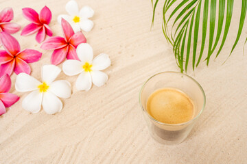 Obraz na płótnie Canvas Black Coffee In Double Wall Glass On sand Beach Next To Palm Leaf And Frangipani Flowers.