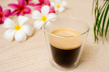 Double Wall Glass Espresso On Sand Beach Next To Frangipani Flowers.