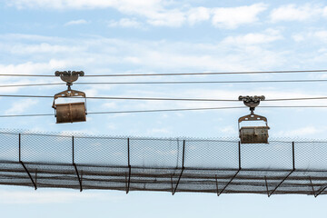 Obraz premium Protected industrial ropeway, on which trolleys move, empty and loaded with raw materials against background of blue summer sky.