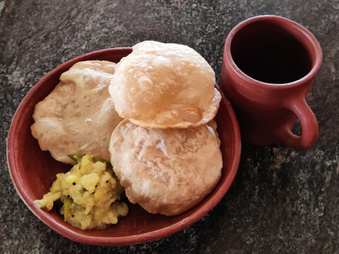 delicious Indian breakfast dish Poori with bhaji curry in a traditional mud plate near to the mud glass isolated on the granite surface
