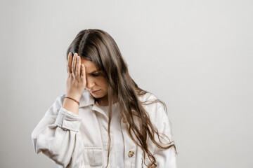 Migraine and headaches in women. Brunette girl with long hair on a gray background