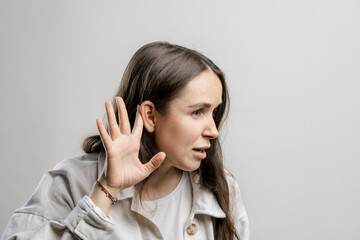 Woman is eavesdropping on a conversation. Brunette girl with long hair on a gray background