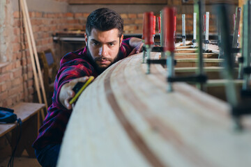 Carpenter sandpapering wooden canoe he is constructing in his workshop