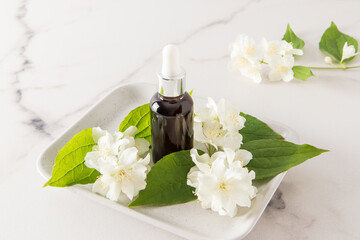 Obraz na płótnie Canvas cosmetic jasmine oil in a glass bottle on a ceramic tray with fresh flowers . care for the skin of the face and body. marble white background.