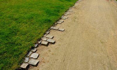 beige gravel material bordered by granite cubes with a serrated pattern. The rough appearance of the historic park follows the gravel path of granite stone cubes around the gutter of the lawn