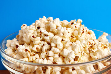 Large transparent bowl filled with popcorn on a blue background.