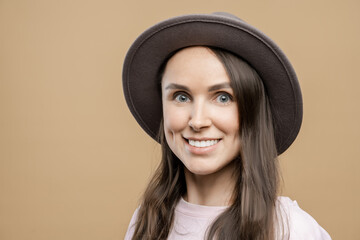 Brunette girl with long hair wearing a hat on a beige background