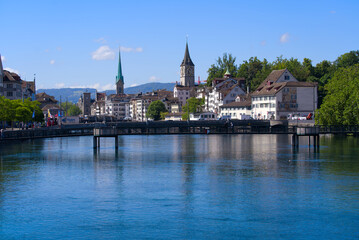 Naklejka na ściany i meble Skyline of the old town of Zürich with churches Women's Minster and St. Peter with river Limmat in the foreground on a blue cloudy summer day. Photo taken June 10th, 2022, Zurich, Switzerland.