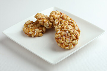 A traditional Indian sweet like bars made from groundnuts and jaggery called Chikki is served on a white plate on a white background