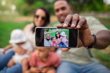 Man's hand holding a smartphone showing a portrait of his biracial family - Powered by Adobe