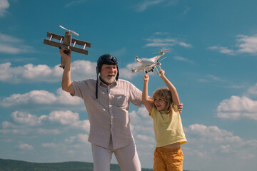 Grandfather and grandson with plane and quadcopter drone over blue sky and clouds background.