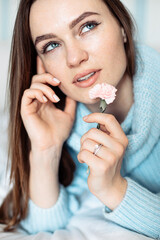 Cute young woman holding delicate flower in hand near face, closeup portrait. Looking at sides, thinking.