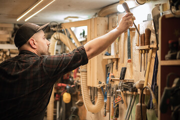 Carpenter holding and putting joinery equipment tools in special frame shelf on the wall. Furniture and repair industry - obrazy, fototapety, plakaty