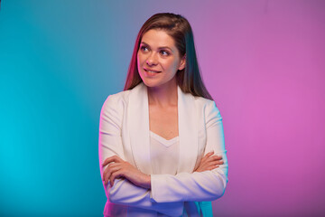 Business woman standing with arms crossed and looking away, portrait with neon lights colors effect. Female model on neon colored background wearing white suit.