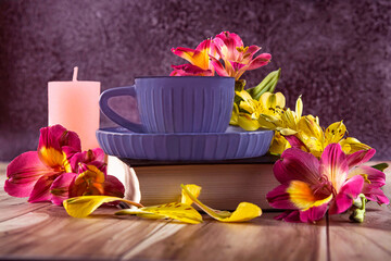 Yellow and purple flowers of alstroemeria, blue cup of coffee. Romantic composition with candles and a book. Bottom view