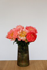 Beautiful bouquet of peonies in a glass vase on table. Visible petal structure. Bright patterns of flower buds. Top view, close up, copy space, white wall background.