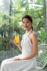 Portrait of a beautiful woman holding a glass of orange juice looking at you sitting at home