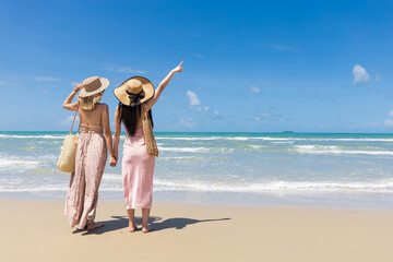 back view women couple standing on the beach and pointing to the sky during summer vacation