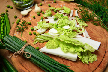 vegetables on a wooden kitchen board, green onions, dill and peas, sliced cabbage on a wood...