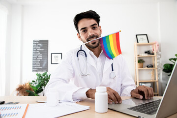 Fototapeta premium LGBT health handsome doctor with rainbow flag. Bisexual, Lesbian and Transgender care concept. Work from home in the bedroom