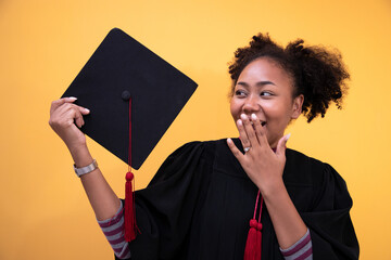 Graduates holding black hats with red tassels standing with raised diploma in yellow studio background. Concept congratulated the graduates in University.