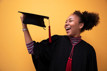 Graduates holding black hats with red tassels standing with raised diploma in yellow studio...