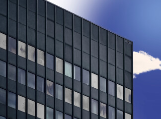 Fototapeta premium Monotonous boring office tower with gray facade made of aluminum in front of surreal blue graded sky with a cloud, minimalist abstraction