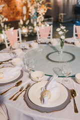 Flower arrangement for summer wedding, made of roses and green branches on a dinner table in the restaurant. , glass and plates in the restaurant outside on a windy day with film grain effect