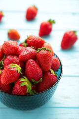 Ripe strawberries in dark blue bowl on blur background. Vertical photo.
