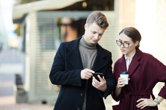 Serious Young Business People Standing On City Street: Man Showing Social Media Outreach On Smartphone To Colleague