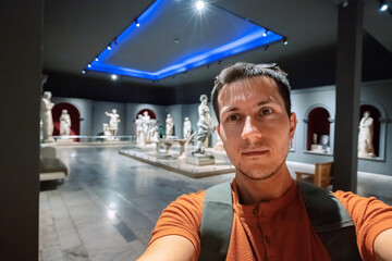  Man taking selfie photo in the hall with Greek antique statues of women and goddesses in the...