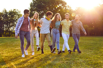 Happy best friends having fun outside in summer. Six joyful beautiful young multiethnic people enjoying good weather, walking on green grass in park, talking, laughing and having great time together