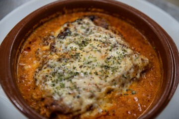 Homemade lasagna baked in a terracotta round pot, individual portion of the traditional Italian dish made of layers of lasagne pasta, delicious ragu sauce, rich bechamel gratin with dried herbs on top