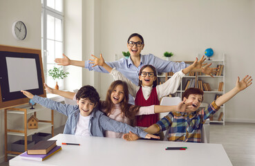 Happy teacher and group of children laughing, shouting hooray and looking at camera. Young woman...