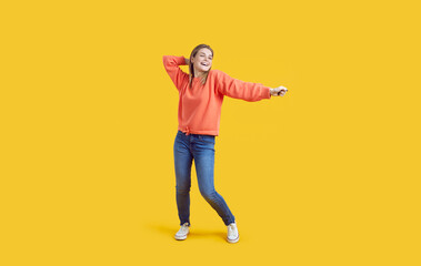 Fototapeta na wymiar Happy beautiful young girl having fun in a modern studio. Full length shot of a cheerful woman in comfortable casual wear laughing and dancing against a vibrant yellow colour background