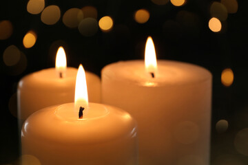 Fototapeta na wymiar Wax candles burning on black background with blurred lights, closeup. Bokeh effect