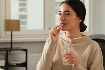 Young woman with glass of water taking dietary supplement pill indoors, space for text - Powered by Adobe