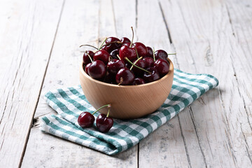 Fresh cherries with water drops in wooden bowl on white wooden table