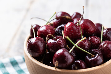 Fresh cherries with water drops in wooden bowl on white wooden table