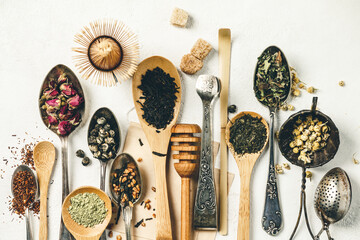 Creative composition with Various kinds of dry tea, silver and bamboo spoons and sugar on white...