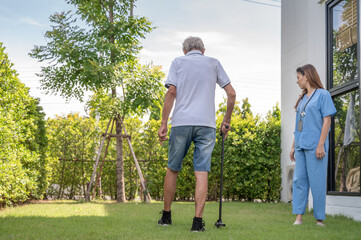 Fototapeta premium Smiling caregiver helping happy elderly man to walk in nursing home