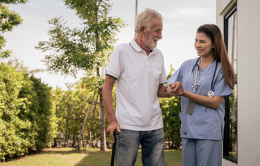 Smiling caregiver helping happy elderly man to walk in nursing home