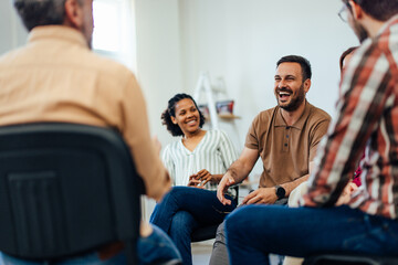Man laughing while talking to the people, sitting in a circle, during the group therapy.