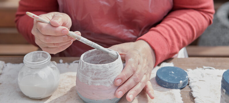 Hands Of Older Woman Painting Handmade Clay Vase With Colored Paints With Brush.