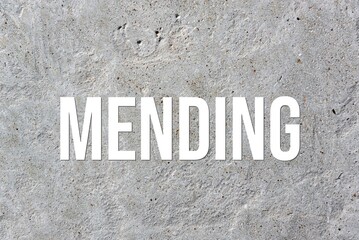MENDING - word on concrete background. Cement floor, wall.