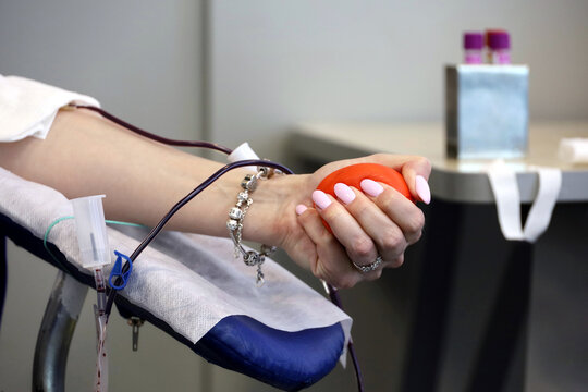 Woman Blood Donor In Chair During Donation With A Blood Bag And Red Bouncy Ball In Hand, Selective Focus. Concept Of Donorship, Transfusion, Health Care