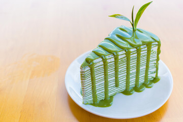 Matcha green tea crepe cake which on top with matcha sauce and decorated with fresh green tea leave put on a white plate on a wooden table. - Powered by Adobe