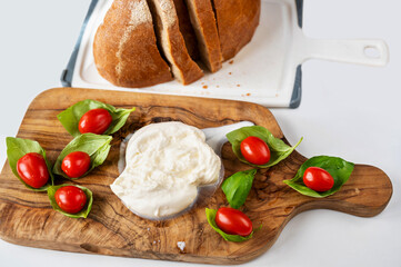 Cherry tomato on green basil leaf, mozzarella and bread on white.