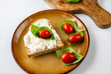 Plate with bread with mozarella and cherry tomato on basil leaf, wooden board on white.