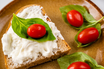 Fototapeta na wymiar Bread with mozarella cheese, cherry tomato on basil leaf on brown plate.